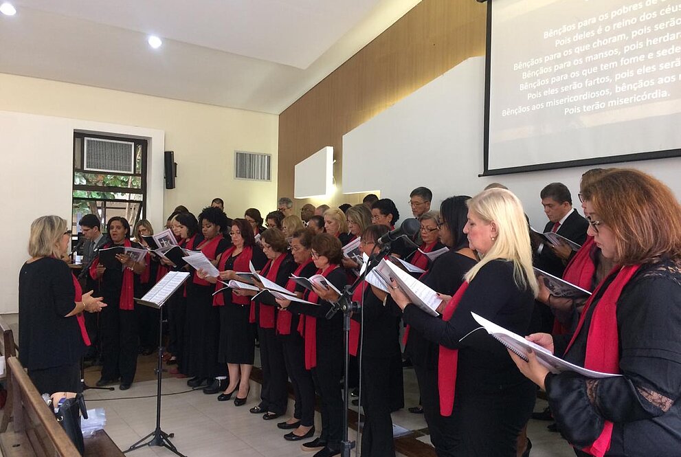 Pessoas do coral de pé todas vestidas de preto e vermelho