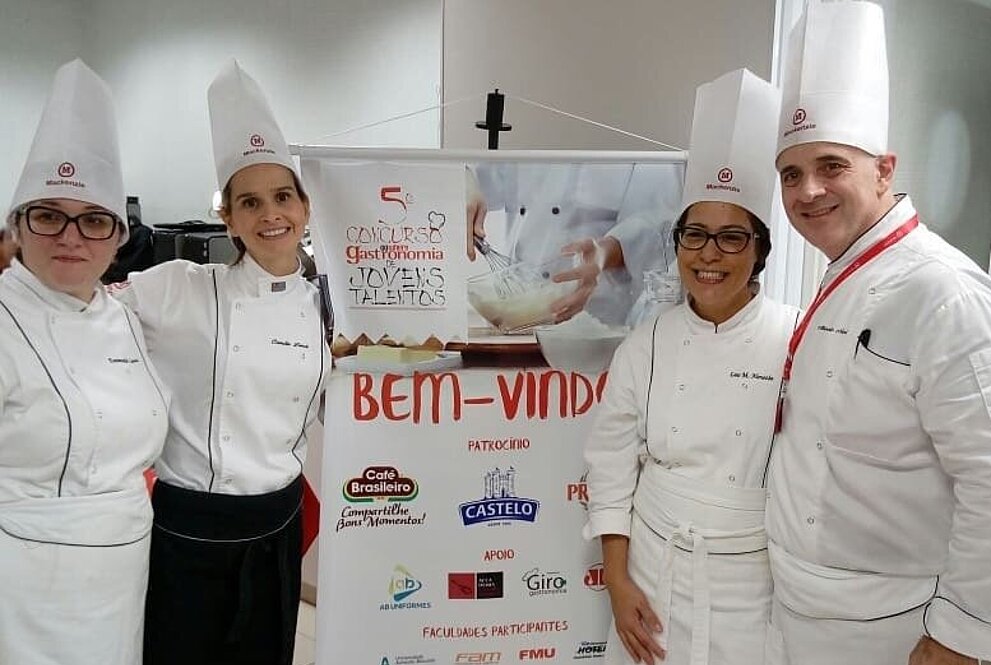 Quatro pessoas sorrindo olhando para a foto e um banner entre  duas pessoas no meio