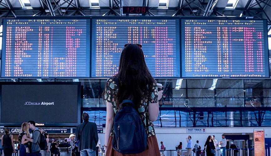 Garota olhando tela de desembarque em aeroporto.