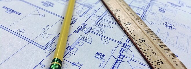 Imagem com um projeto de arquitetura desenhado no papel e junto com um lápis e uma régua
