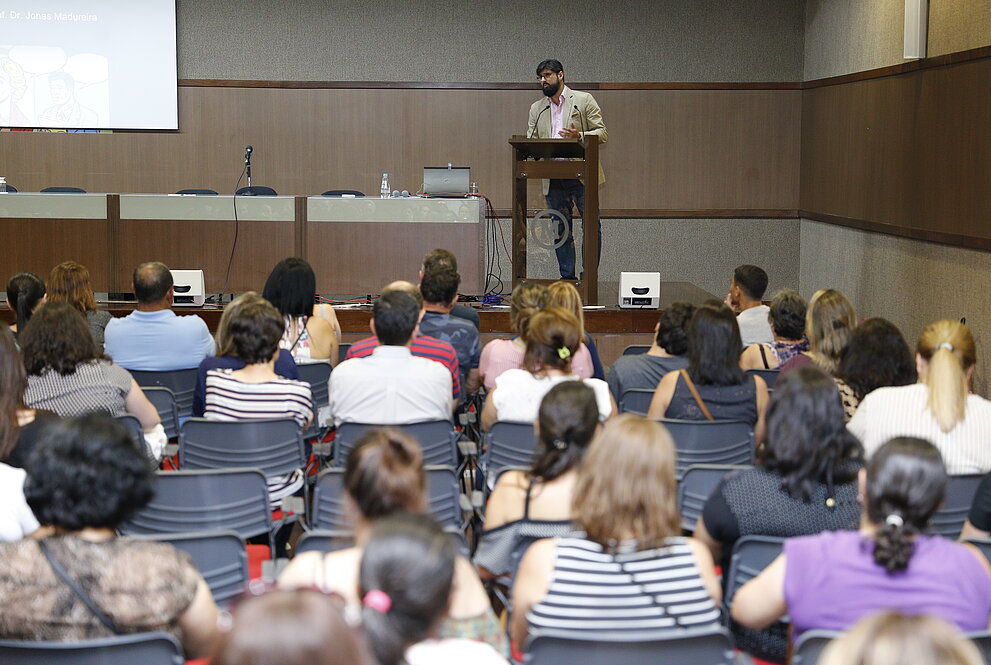 Professor sobre palco se apresenta para plateia